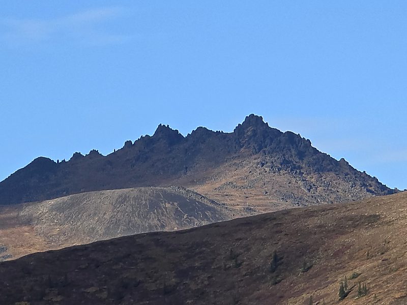 Jagged rocky mountain summit above dark autumn hillsides against a clear blue sky
